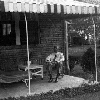 Man seated on porch, relaxing in a vintage setting.