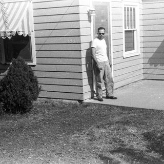 Man stands near a house with awnings and greenery.