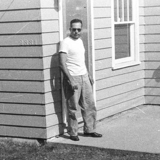 Man stands near a house with awnings and greenery.