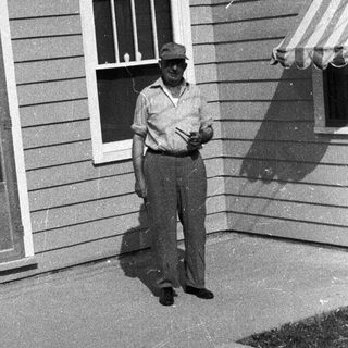 Man stands outside a house, partially shaded by an awning.