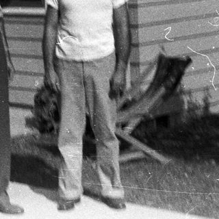 Two men stand outside a modest, older house.