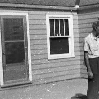 Two men stand outside a modest, older house.