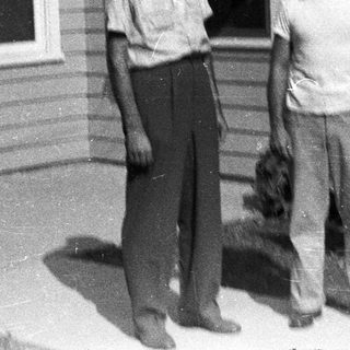 Two men stand outside a modest, older house.