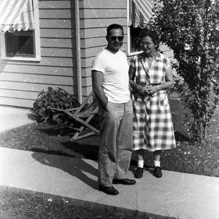 Couple stands outside a vintage home with a garden.