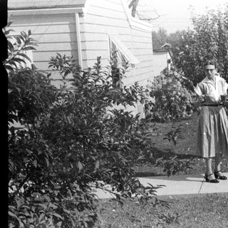 Woman stands on sidewalk near vintage car and house.