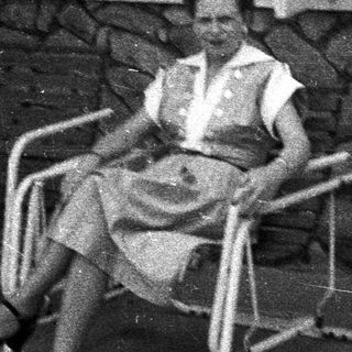 Woman sits on chair, posing in front of stone wall.