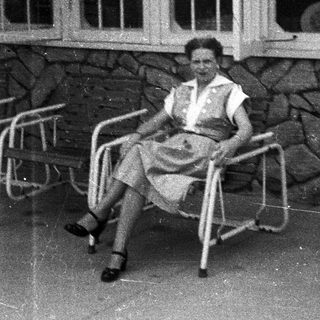 Woman sits on chair, posing in front of stone wall.