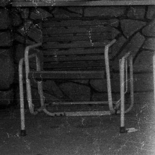 Woman sits on a chair outside a stone building.