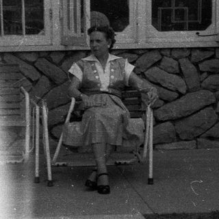 Woman sits on a chair outside a stone building.