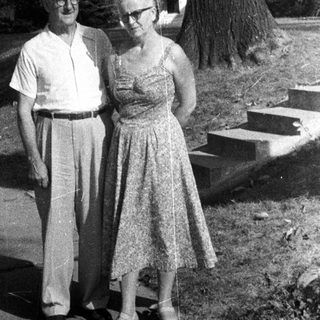 Older couple stands outside a house in black and white.