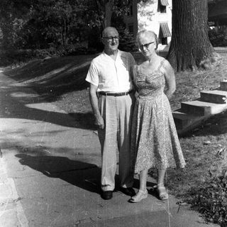 Older couple stands outside a house in black and white.
