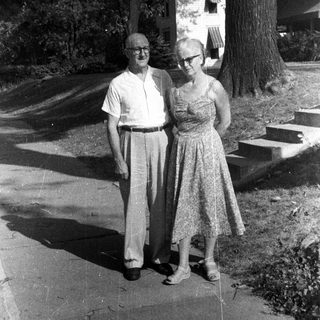 Older couple stands outside a house in black and white.
