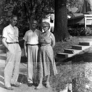 Black and white photo of a family standing near a house.