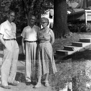 Black and white photo of a family standing near a house.