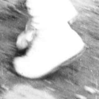 Here's a brief summary of the image: Child stands at a vintage fountain, reaching for water.