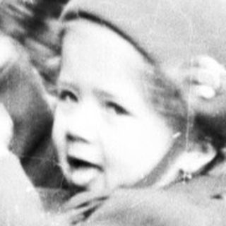 Here's a brief summary of the image: Child stands at a vintage fountain, reaching for water.