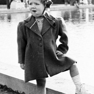 Here's a brief summary of the image: Young child in coat stands near a pond.