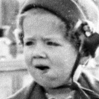 Here's a brief summary of the image: Young child in coat stands near a pond.