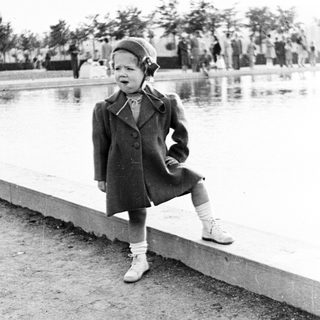 Here's a brief summary of the image: Young child in coat stands near a pond.
