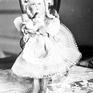 Antique doll posed on a vase, black and white.