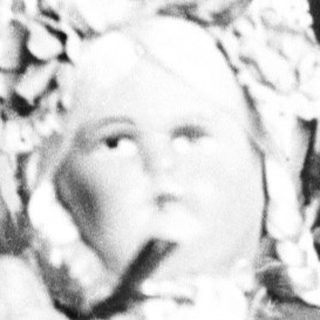 Antique doll posed on a vase, black and white.