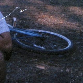 Man sits near tent in a wooded campsite.