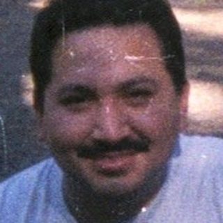 Man sits near tent in a wooded campsite.