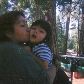 Woman holding and kissing a child outdoors in a forest.