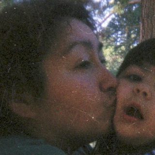 Woman holding and kissing a child outdoors in a forest.