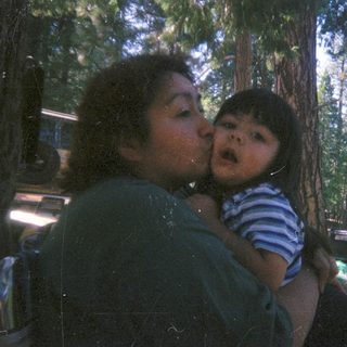 Woman holding and kissing a child outdoors in a forest.