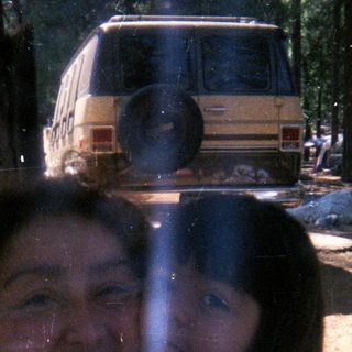 Girl looking through a window, camping scene in background.