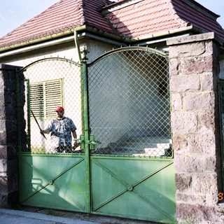 Man stands by a gated building with a red roof.