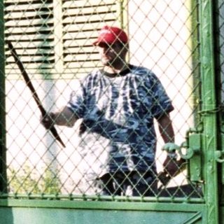 Man stands by a gated building with a red roof.