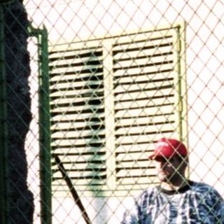 Man stands by a gated building with a red roof.