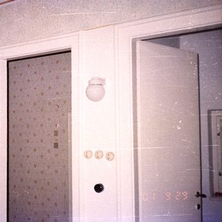 Man holding baby in doorway with wallpaper and light fixture.