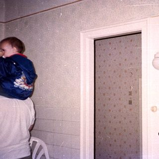 Man holding baby in doorway with wallpaper and light fixture.