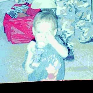 Man in camo pants stands near a child in a kitchen.