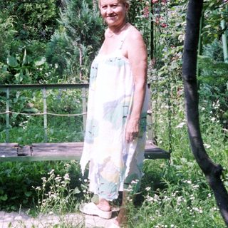 Woman stands near a swing in a lush garden.