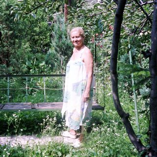 Woman stands near a swing in a lush garden.