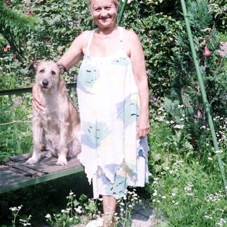 Woman and dog stand in a lush, vibrant garden.