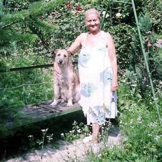 Woman and dog stand in a lush, vibrant garden.