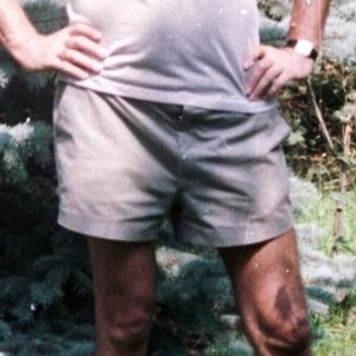 Man stands in a garden near a pine tree.