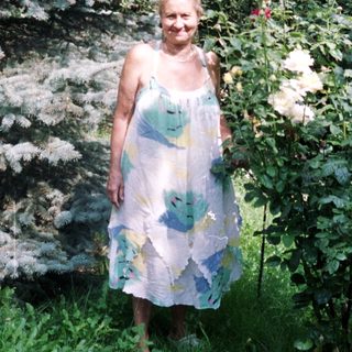 Woman stands in a garden with spruce trees and roses.