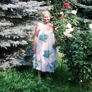 Woman stands in a garden with spruce trees and roses.