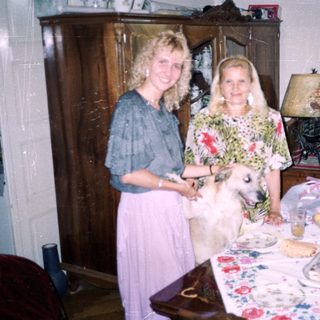 Two women and a dog stand near a table indoors.