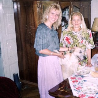 Two women and a dog stand near a table indoors.
