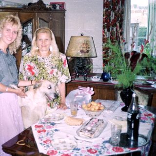 Two women and a dog stand near a table indoors.