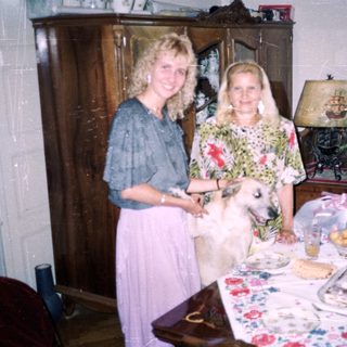 Two women and a dog stand near a table indoors.