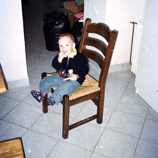 Young child sits on a chair in a tiled room.