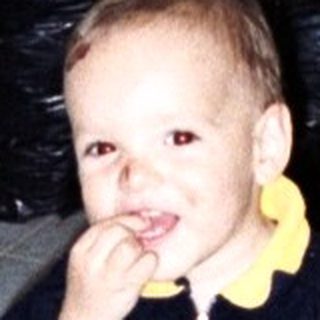 Young child sits on a chair in a tiled room.